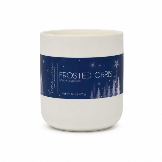 A white ceramic candle jar with a navy blue holiday-themed paper label reading 'FROSTED ORRIS' and 'Holiday Collection' by Dina Essential, shown on a white background.