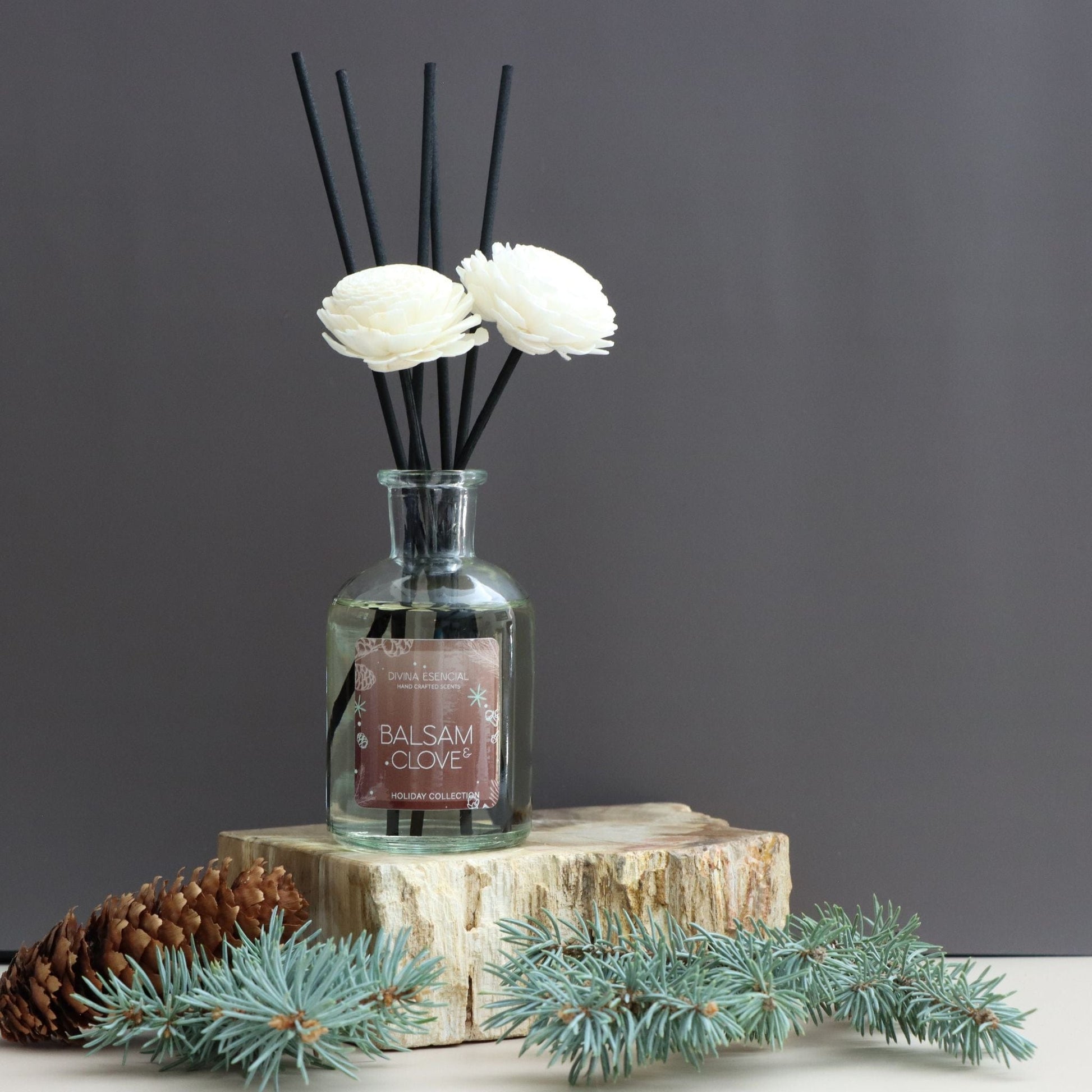 Diffuser with floral reeds and decorative elements on a wooden block against a dark background