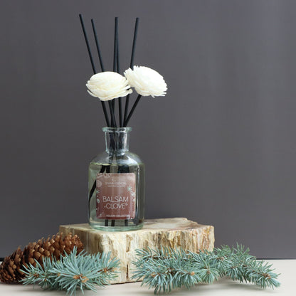 Diffuser with floral reeds and decorative elements on a wooden block against a dark background