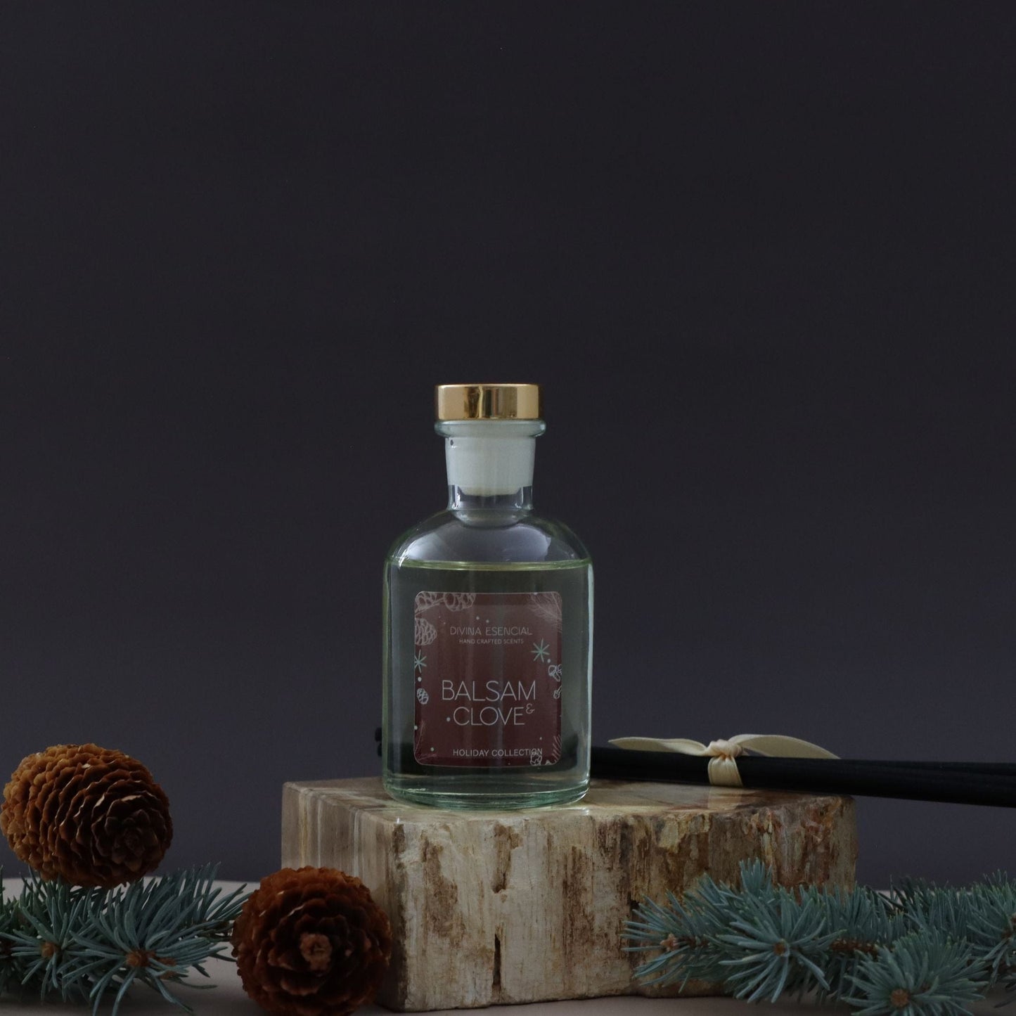 Bottle of Balsam Clove on a wooden block with pine cones and branches against a dark background