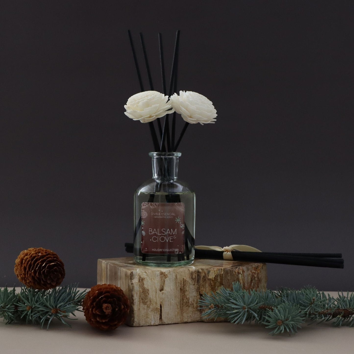 A glass diffuser bottle with floral elements on a wooden block against a dark background